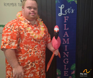 Guy posing with inflatable flamingo next to sign that says 'Let's flamingle'