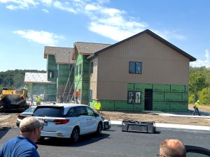 IMG_0403 - The Arc Fayette Construction site with a partially built two-story house, green exterior sheathing, and workers in neon vests under a blue sky